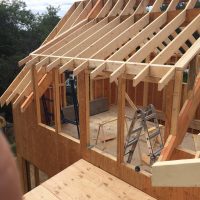 Partially constructed wooden house frame with exposed rafters and an aluminum ladder inside the structure.