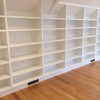 Empty white built-in bookshelves line a wall above a wooden floor in a well-lit room.