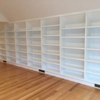 White built-in bookshelves line a wall in a room with light wood flooring and a sloped ceiling.