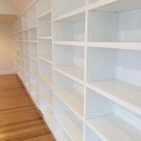 White, empty built-in bookshelves line a room with light wood flooring and plain white walls.