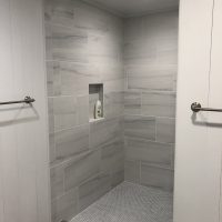 Modern walk-in shower with gray tiles, built-in niche holding shampoo, and two towel bars on either side.