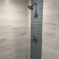 Shower with a silver showerhead and faucet, featuring white tiles and a vertical strip of blue accent tiles.