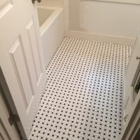 Bathroom with white woven-pattern tile floor, white door, bathtub with white tile, and a window above the tub.
