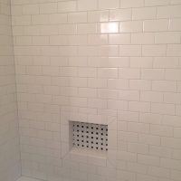 White tiled bathroom wall with a recessed niche featuring a small black and white tile pattern in the center.