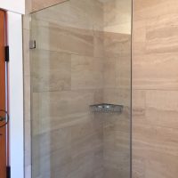 Glass shower enclosure with beige tiled walls and a metal wire shelf in the corner.