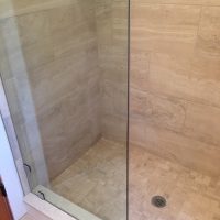 A tiled walk-in shower with a glass door, corner drain, and a metal shelf mounted on the wall.