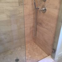 Glass-enclosed shower with beige tile walls, handheld showerhead, and chrome fixtures.