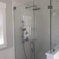 Glass shower with chrome fixtures, a rainfall showerhead, and a handheld sprayer in a white-tiled bathroom.