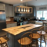 Modern kitchen with gray cabinets, wooden island, stainless steel appliances, and four wooden chairs.