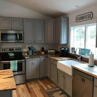 Modern farmhouse kitchen with gray cabinets, wood countertops, stainless appliances, and a large white farmhouse sink.