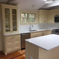 Modern kitchen with cream cabinets, stainless steel appliances, white countertops, and a window above the sink.