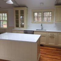 A kitchen with cream-colored cabinets, a white island, stainless steel appliances, and wood floors.