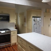 Modern kitchen with cream cabinets, stainless steel appliances, and a white marble island; living room in background.