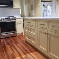 Modern kitchen with cream cabinets, stainless steel oven, white countertops, and wood flooring.